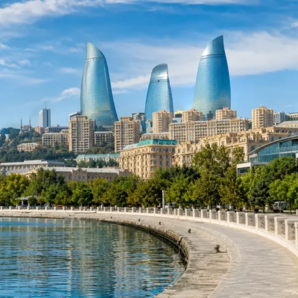 Bright daytime view of Baku waterfront with the iconic Flame Towers, tree-lined promenade, and calm Caspian shoreline.