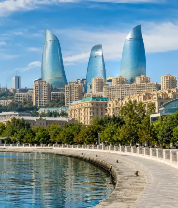 Bright daytime view of Baku waterfront with the iconic Flame Towers, tree-lined promenade, and calm Caspian shoreline.
