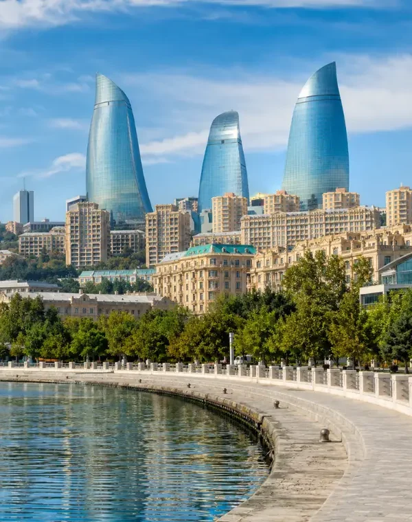 Bright daytime view of Baku waterfront with the iconic Flame Towers, tree-lined promenade, and calm Caspian shoreline.