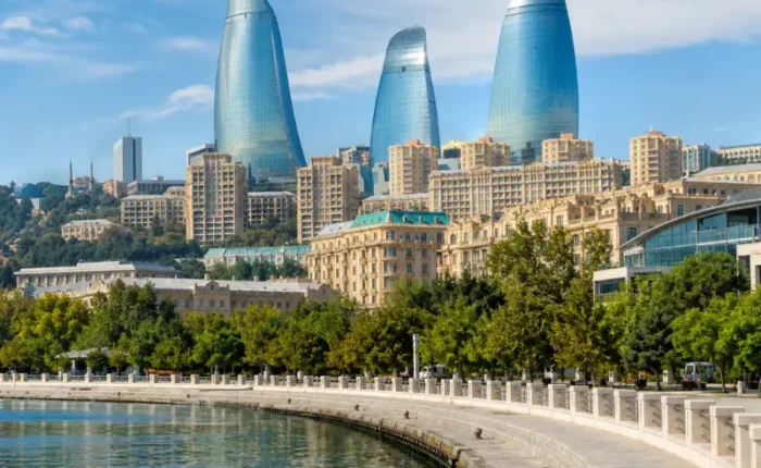 Bright daytime view of Baku waterfront with the iconic Flame Towers, tree-lined promenade, and calm Caspian shoreline.