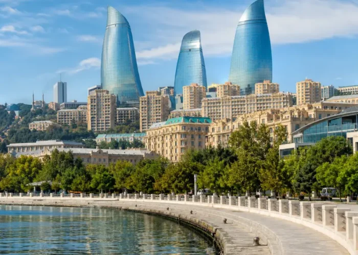 Bright daytime view of Baku waterfront with the iconic Flame Towers, tree-lined promenade, and calm Caspian shoreline.