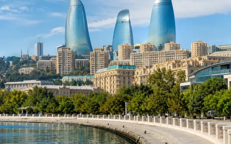 Bright daytime view of Baku waterfront with the iconic Flame Towers, tree-lined promenade, and calm Caspian shoreline.