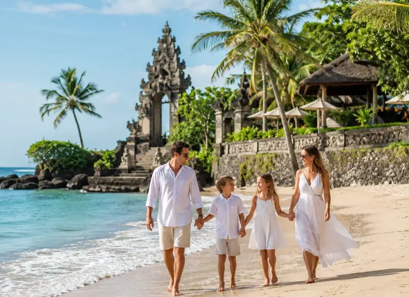 Family enjoying Bali beach with turquoise sea, golden sand, palm trees, and Balinese resort architecture.
