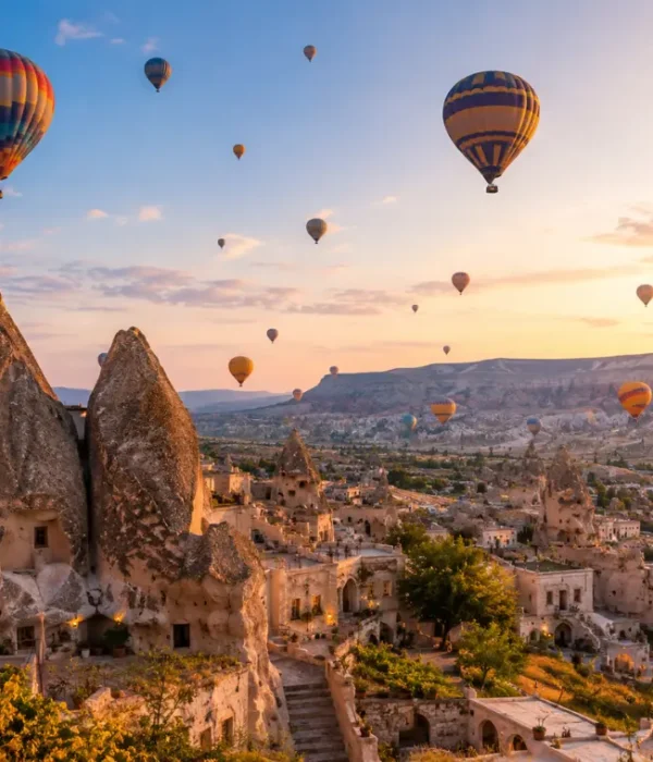 Scenic view of Cappadocia with fairy chimney rock formations, cave houses, and colorful hot air balloons in the sky.