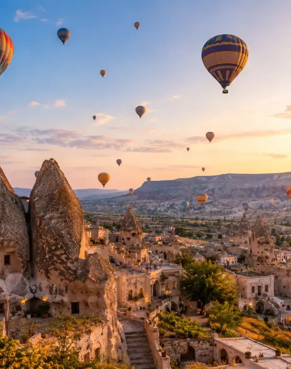 Scenic view of Cappadocia with fairy chimney rock formations, cave houses, and colorful hot air balloons in the sky.
