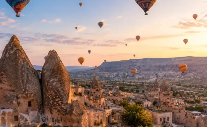 Scenic view of Cappadocia with fairy chimney rock formations, cave houses, and colorful hot air balloons in the sky.