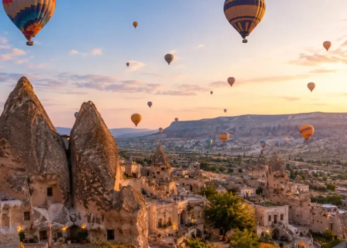 Scenic view of Cappadocia with fairy chimney rock formations, cave houses, and colorful hot air balloons in the sky.