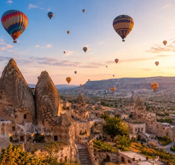 Scenic view of Cappadocia with fairy chimney rock formations, cave houses, and colorful hot air balloons in the sky.