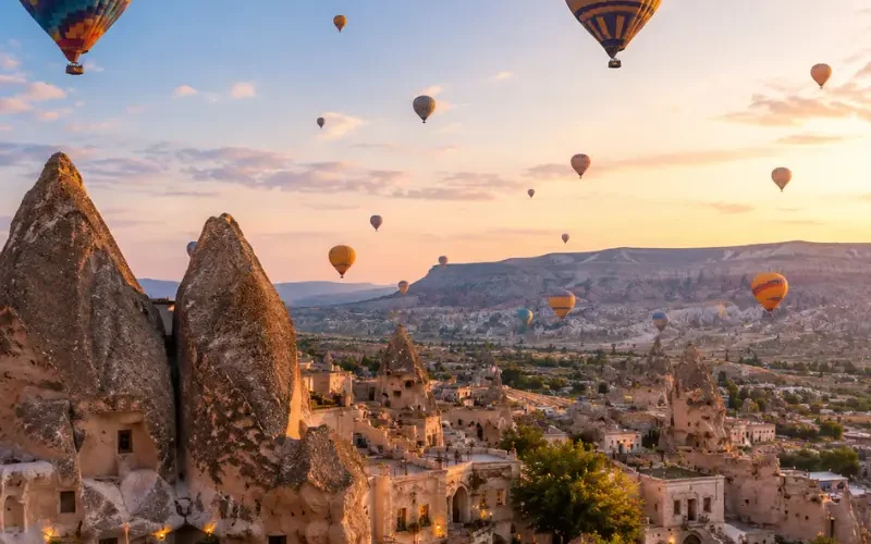 Scenic view of Cappadocia with fairy chimney rock formations, cave houses, and colorful hot air balloons in the sky.