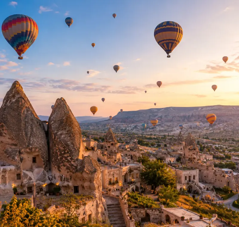 Scenic view of Cappadocia with fairy chimney rock formations, cave houses, and colorful hot air balloons in the sky.