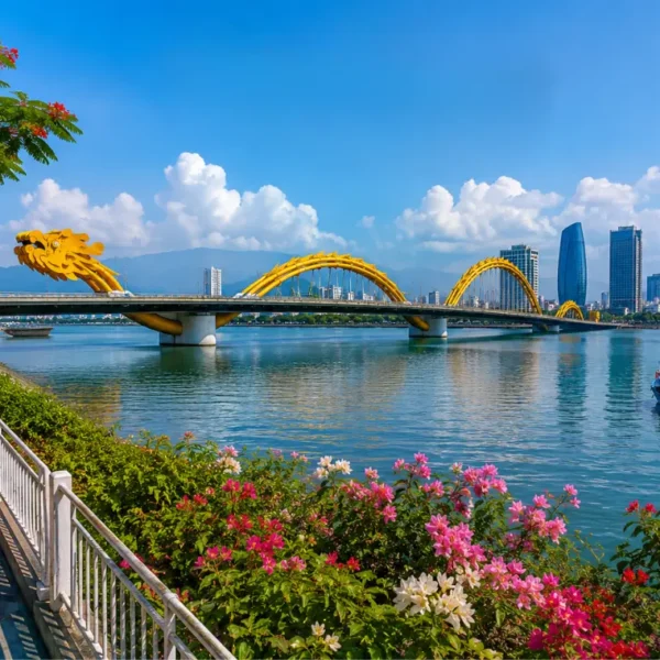 Da Nang, Vietnam skyline with Dragon Bridge, Han River, riverside flowers, boats, and clear blue daytime sky.