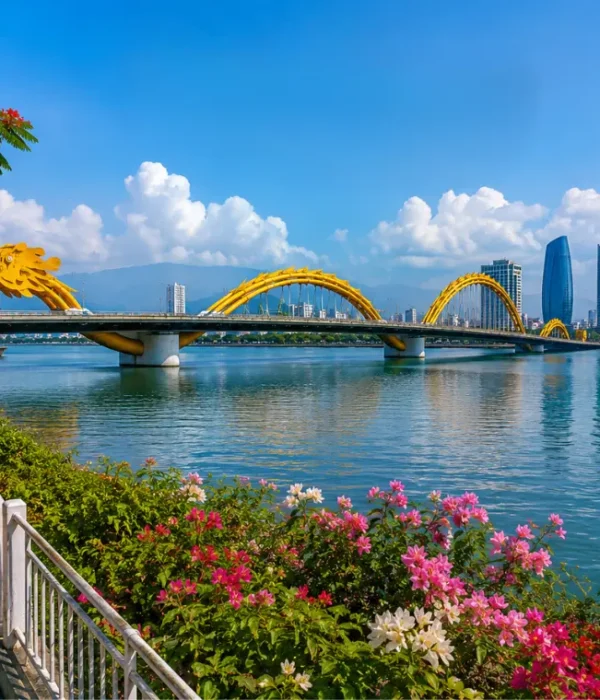Da Nang, Vietnam skyline with Dragon Bridge, Han River, riverside flowers, boats, and clear blue daytime sky.