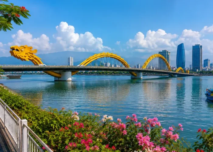 Da Nang, Vietnam skyline with Dragon Bridge, Han River, riverside flowers, boats, and clear blue daytime sky.