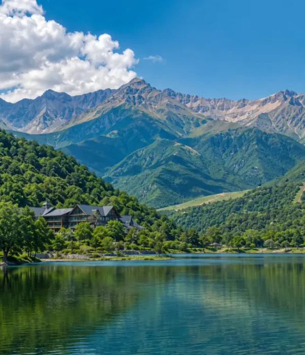 Scenic daytime view of Gabala with a calm lake, lush green hills, mountain resort, and the Caucasus peaks in the background.