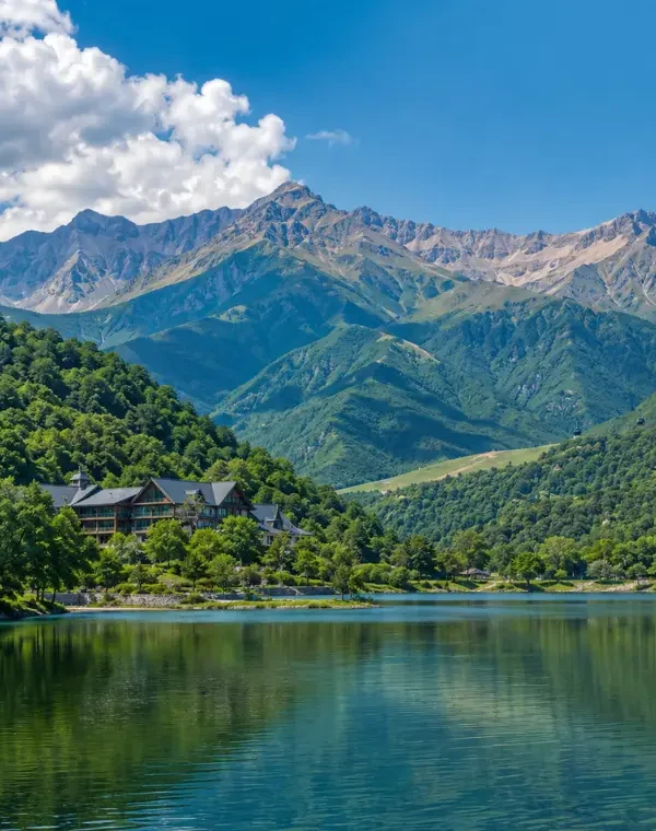 Scenic daytime view of Gabala with a calm lake, lush green hills, mountain resort, and the Caucasus peaks in the background.
