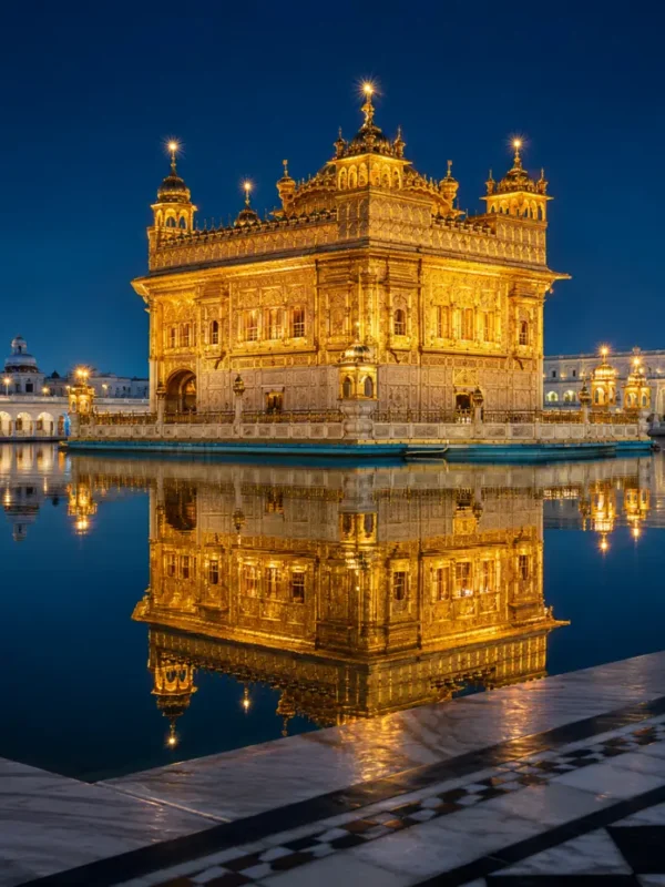 Golden Temple in Amritsar glowing at night with golden lights, calm water reflection, marble walkway, and a luxury spiritual travel atmosphere.