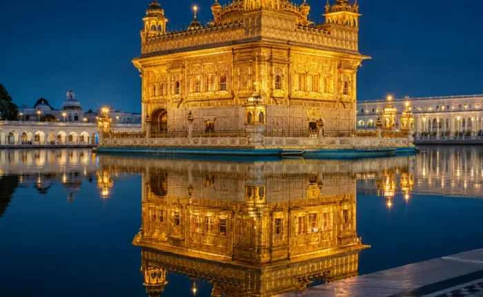 Golden Temple in Amritsar glowing at night with golden lights, calm water reflection, marble walkway, and a luxury spiritual travel atmosphere.
