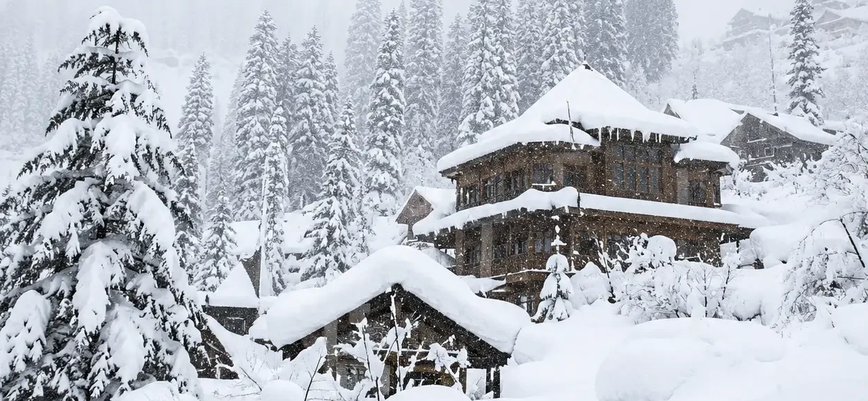 Snow-covered Manali hillside with pine trees and traditional wooden cottages in Himachal Pradesh