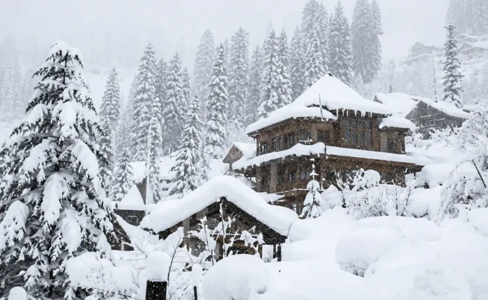 Snow-covered Manali hillside with pine trees and traditional wooden cottages in Himachal Pradesh