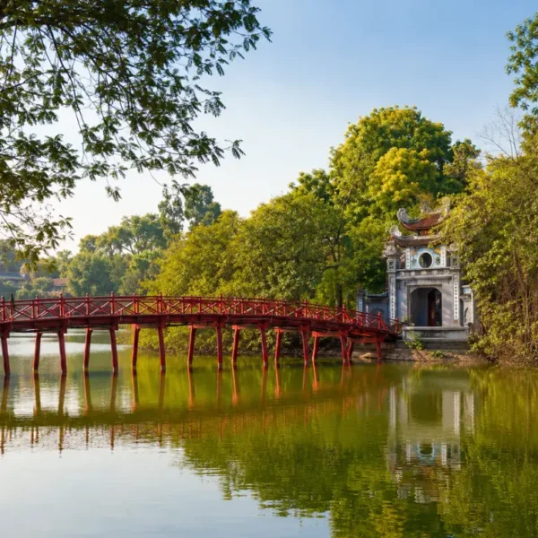 Hoan Kiem Lake in Hanoi with red The Huc Bridge, Ngoc Son Temple, calm water, and lush green trees.