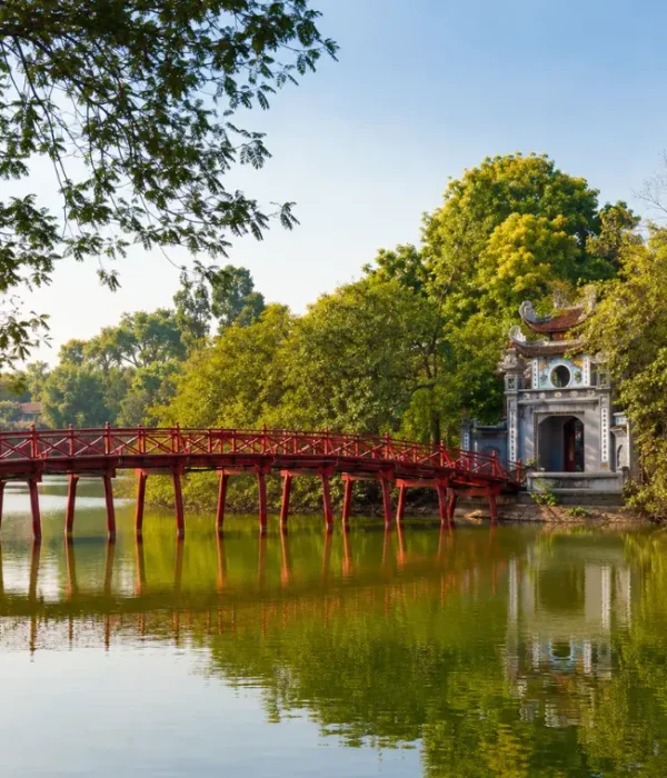 Hoan Kiem Lake in Hanoi with red The Huc Bridge, Ngoc Son Temple, calm water, and lush green trees.