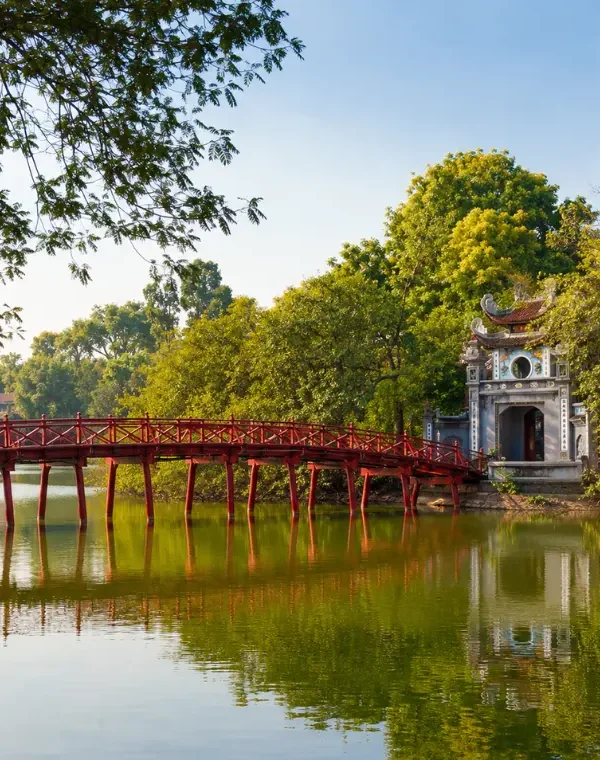 Hoan Kiem Lake in Hanoi with red The Huc Bridge, Ngoc Son Temple, calm water, and lush green trees.