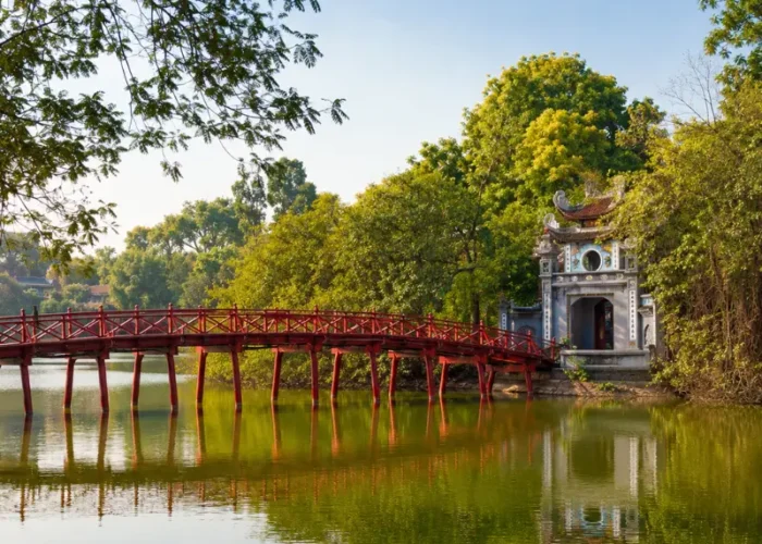 Hoan Kiem Lake in Hanoi with red The Huc Bridge, Ngoc Son Temple, calm water, and lush green trees.