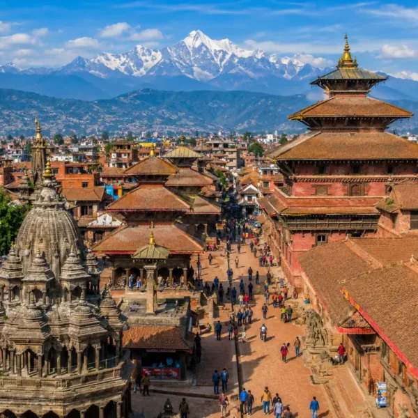 Bright daytime view of Kathmandu with traditional temples, historic square, city rooftops, and Himalayan mountains.