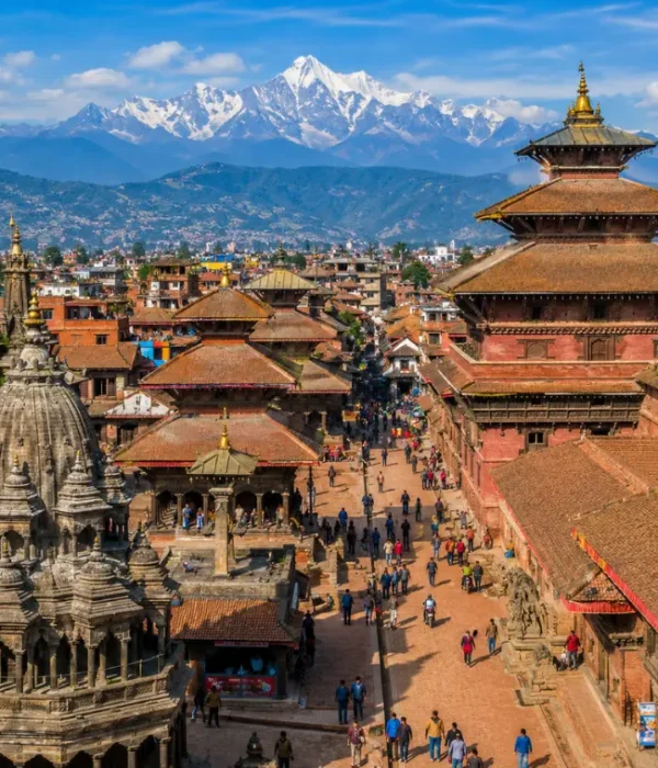 Bright daytime view of Kathmandu with traditional temples, historic square, city rooftops, and Himalayan mountains.