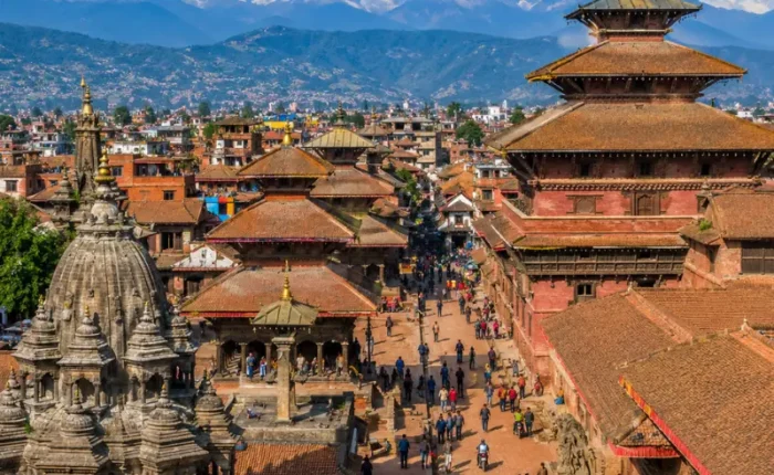 Bright daytime view of Kathmandu with traditional temples, historic square, city rooftops, and Himalayan mountains.