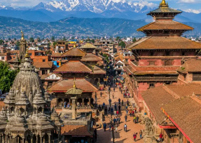 Bright daytime view of Kathmandu with traditional temples, historic square, city rooftops, and Himalayan mountains.