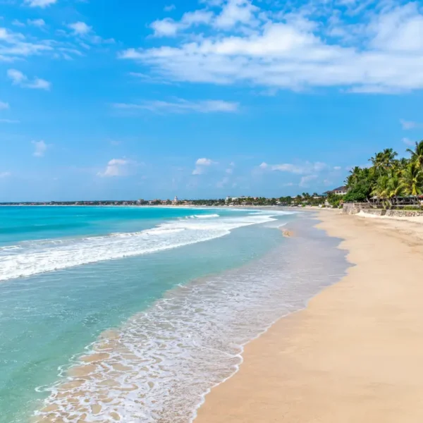 Kuta Beach in Bali with turquoise waves, golden sand, palm trees, and clear blue daytime sky.