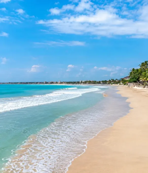 Kuta Beach in Bali with turquoise waves, golden sand, palm trees, and clear blue daytime sky.