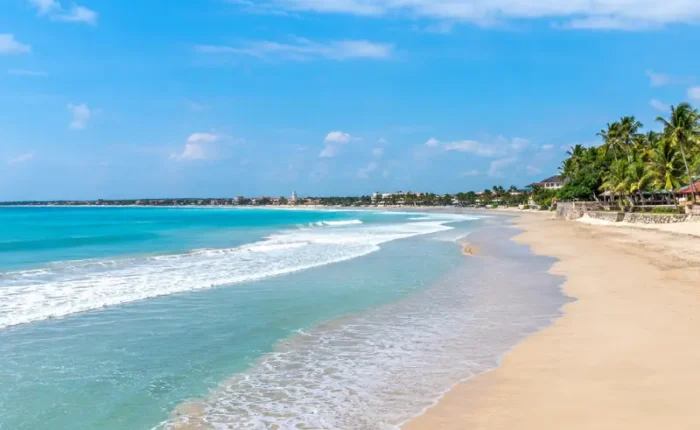 Kuta Beach in Bali with turquoise waves, golden sand, palm trees, and clear blue daytime sky.