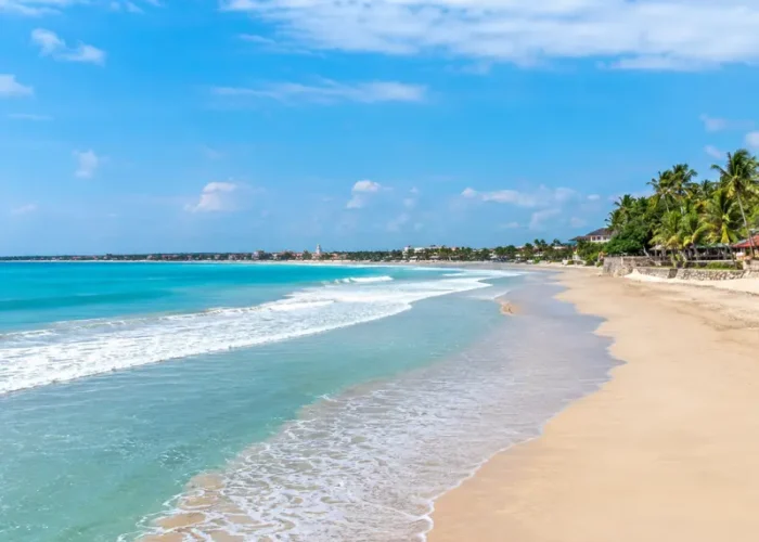 Kuta Beach in Bali with turquoise waves, golden sand, palm trees, and clear blue daytime sky.