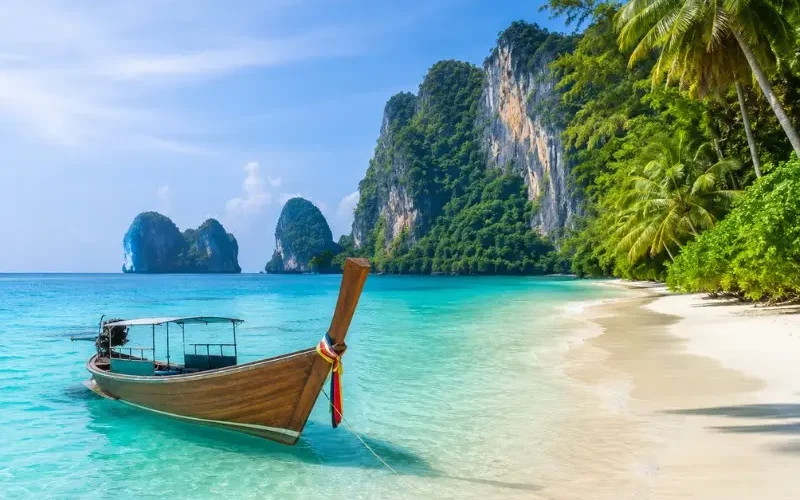 Phuket Island beach with turquoise water, long-tail boat, white sand and tropical limestone cliffs