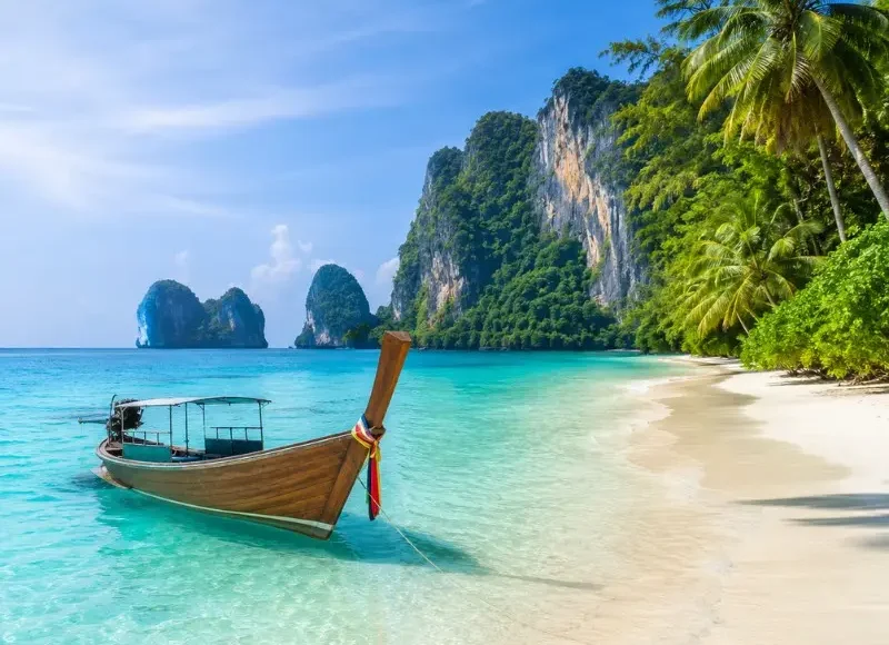 Phuket Island beach with turquoise water, long-tail boat, white sand and tropical limestone cliffs
