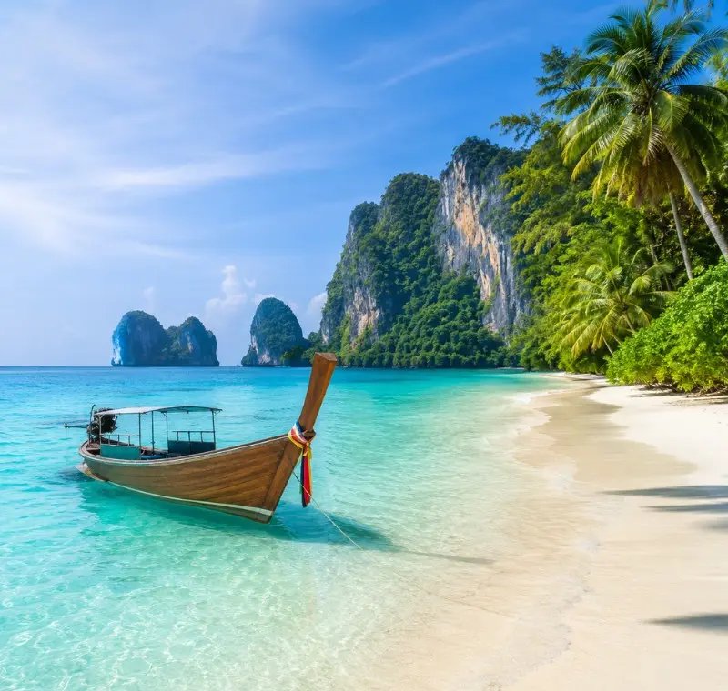Phuket Island beach with turquoise water, long-tail boat, white sand and tropical limestone cliffs