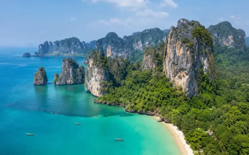 Krabi coastline with turquoise sea, limestone cliffs, white sand beach and tropical greenery in daylight