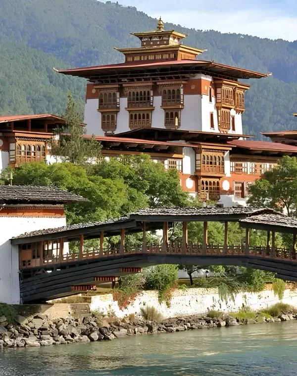 Punakha Dzong in Bhutan with traditional bridge, riverside architecture, forested mountains, and calm water.