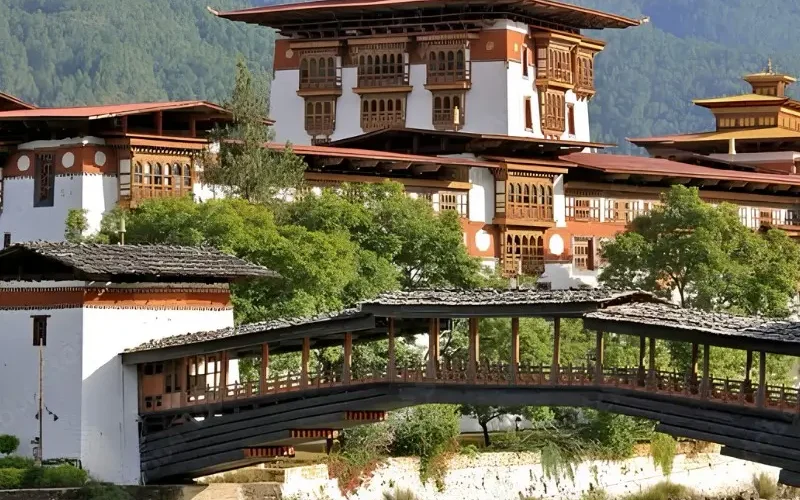 Punakha Dzong in Bhutan with traditional bridge, riverside architecture, forested mountains, and calm water.