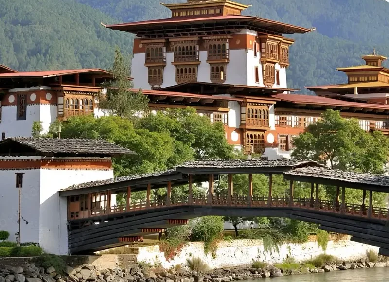 Punakha Dzong in Bhutan with traditional bridge, riverside architecture, forested mountains, and calm water.