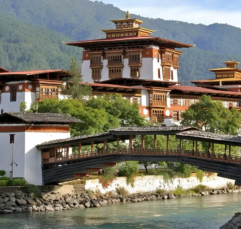 Punakha Dzong in Bhutan with traditional bridge, riverside architecture, forested mountains, and calm water.