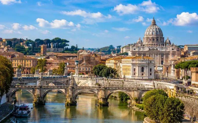 Rome skyline with St. Peter’s Basilica, historic bridge, Tiber River reflections, and warm golden evening light.