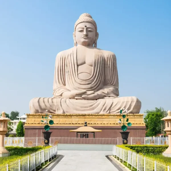 Bodh Gaya travel image featuring a large seated Buddha statue, landscaped gardens, clear blue sky, and peaceful Buddhist pilgrimage surroundings.