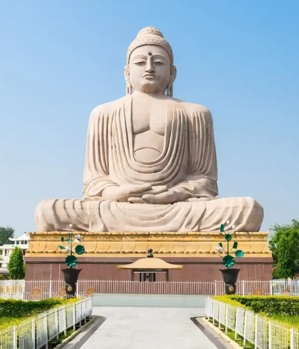 Bodh Gaya travel image featuring a large seated Buddha statue, landscaped gardens, clear blue sky, and peaceful Buddhist pilgrimage surroundings.