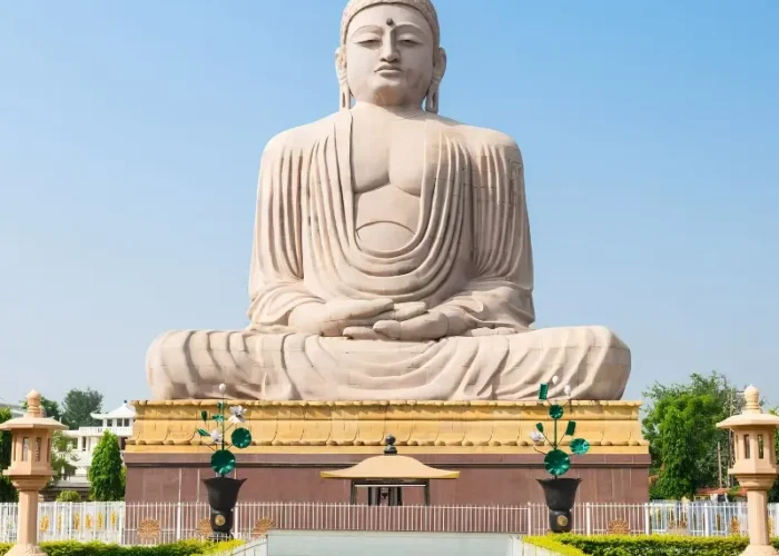 Bodh Gaya travel image featuring a large seated Buddha statue, landscaped gardens, clear blue sky, and peaceful Buddhist pilgrimage surroundings.