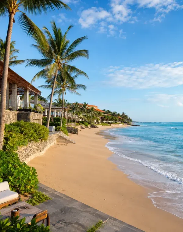 Seminyak, Bali beachfront with golden sand, turquoise sea, swaying palm trees, and luxury seaside villas in clear daylight.