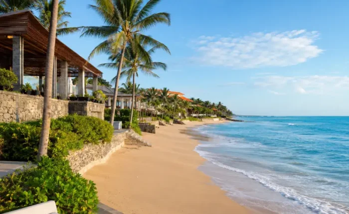 Seminyak, Bali beachfront with golden sand, turquoise sea, swaying palm trees, and luxury seaside villas in clear daylight.