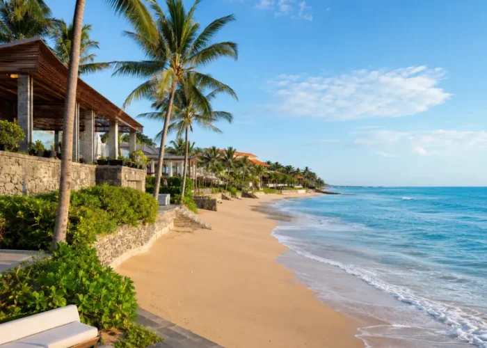 Seminyak, Bali beachfront with golden sand, turquoise sea, swaying palm trees, and luxury seaside villas in clear daylight.